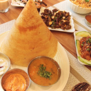 A table displaying Tasty sambar, Coconut chutney, and variety dosas on white plates.