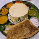 A plate containing a variety of Indian dishes, including samosas, rice, naan, and curry recipes.