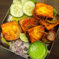 Slices of cucumber, onion, lemon & a bowl of green sauce are offered with a platter of paneer tikka.
