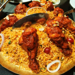 A large plate full of appetizing chicken biryani and multiple chunks of chicken pieces with onions.