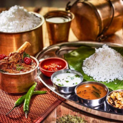 A bowl of rice is served in a banana leaf along with chettinad chicken gravy, pepper water and curd.