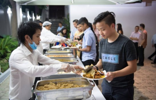 A young man with a happy face serves delicious food to a group of people at the buffet table.