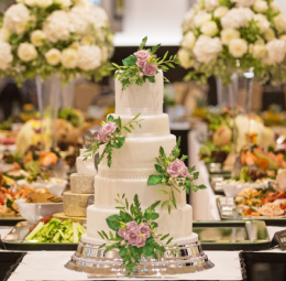 A large cake placed on a wooden table, decorated with a bouquet of various flowers in a glass vase.