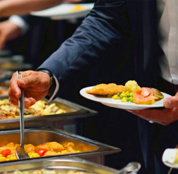 At a buffet, a man holds a colorful plate filled with a variety and delicious food with happy manner