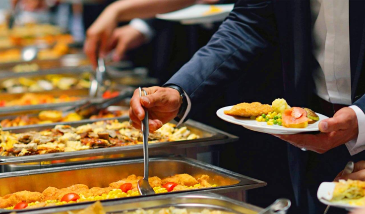 People serve a variety of delicious food at a buffet line during a special occasion for the office.