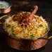 A generous serving of rice biriyani and chicken leg pieces, topped with a flavorful sauce and spices