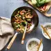 A table with a wok filled with colorful vegetables and a pair of chopsticks resting on top