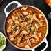 A bowl of delicious seafood and a spoon are placed next to a cooking skillet full of seafood