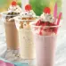 Chocolate, strawberry, and vanilla flavors of milkshakes topped with whipped cream and a cherry.