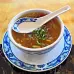 A spoon resting above a bowl of vegetable soup, waiting to be enjoyed and thoroughly tasted